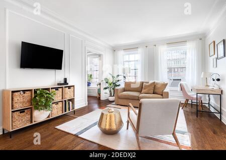Ein helles, weißes Wohnzimmer in einer Downtown-Wohnung mit gemütlichen Möbeln, einem Fernseher an der Wand und einem Teppich auf Hartholzböden. Stockfoto