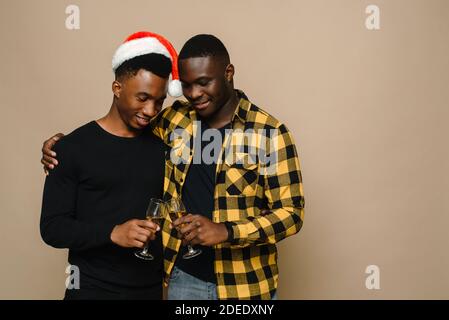 Happy Familie Porträt auf Weihnachten, Gay männliche Paar auf beigem Hintergrund. Ein Paar schwarze Männer in der Liebe clink Gläser Champagner. Prost. Feiern Sie Weihnachten und Neujahr. Stockfoto