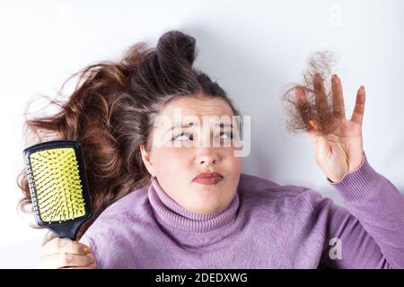 Trauriges junges Mädchen, das lockere Haare in der Hand hält, auf weißem Hintergrund. Stockfoto