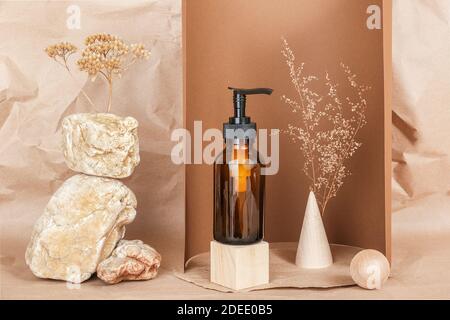 Braune Glasflasche mit Pumpe von kosmetischen Produkten auf Holz geometrischen Formen, Steinen und getrockneten Blumen auf beigem Papier Hintergrund. Natürliches Organisches Spa Stockfoto