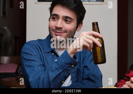Junger attraktiver Mann mit einer Bierflasche in der Hand lächelnd in einer Kneipe. Bar-Konzept. Stockfoto