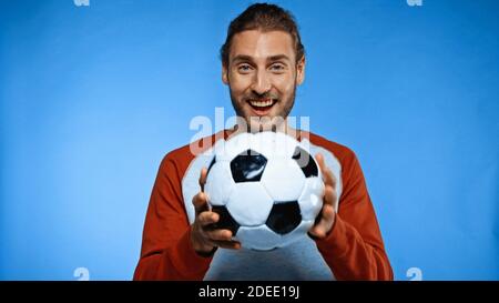 Positiver Fußballfan hält Fußball auf blau Stockfoto
