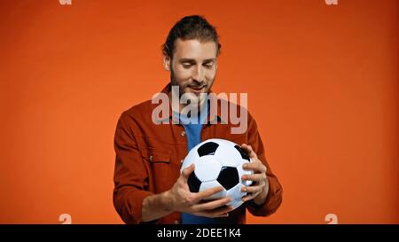 Fröhlicher Fußballfan, der Fußball auf Orange anschaut Stockfoto