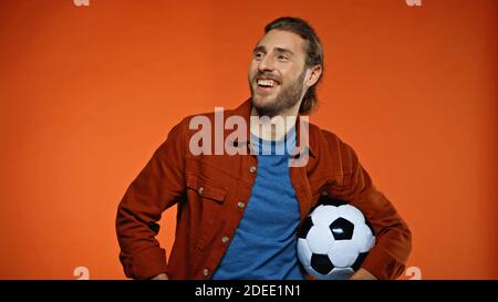 Glücklicher Fußballfan, der wegschaut und den Fußball anhält Orange Stockfoto