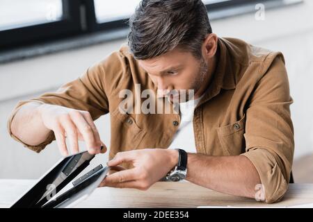 Fokussierter Geschäftsmann Reparatur beschädigt Laptop während sitzen am Tisch auf Unscharfer Hintergrund Stockfoto