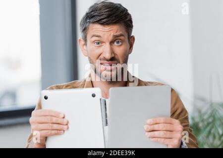 Verwirrt Geschäftsmann Blick auf die Kamera, während halten gebrochen Laptop verschwommen Hintergrund Stockfoto