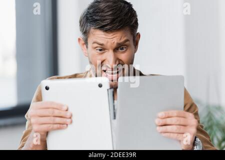 Erschrocken Geschäftsmann Blick auf gebrochene Laptop auf verschwommenem Hintergrund Stockfoto