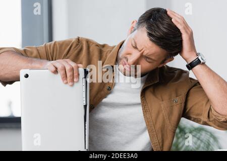 Besorgt Geschäftsmann denken, während Blick auf defekte Laptop auf verschwommen Hintergrund Stockfoto