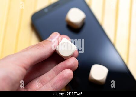 Hand hält eine einfache leere Holzwürfel, leere Würfel mit einem Kreis Logo Kopie Raum in der Mitte über einem modernen Smartphone, Handy mit zwei mehr Stockfoto