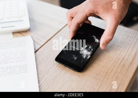 Beschnittene Ansicht des Mannes Putting zerschmetterte Smartphone auf dem Tisch auf Unscharfer Hintergrund Stockfoto