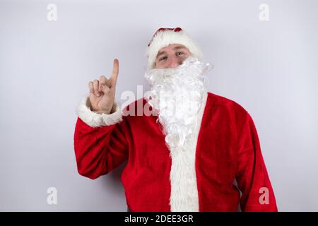 Mann als Weihnachtsmann gekleidet, der über einem isolierten weißen Hintergrund steht und eine Idee hat. Stockfoto