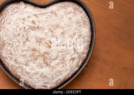 Herzförmiger Kuchen in Springform, frisch gebacken und mit Puderzucker bestäubt Stockfoto