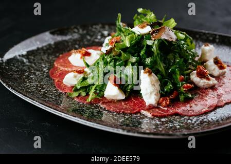 Carpaccio aus Rindfleisch aus Marmor auf schwarzem Hintergrund Stockfoto