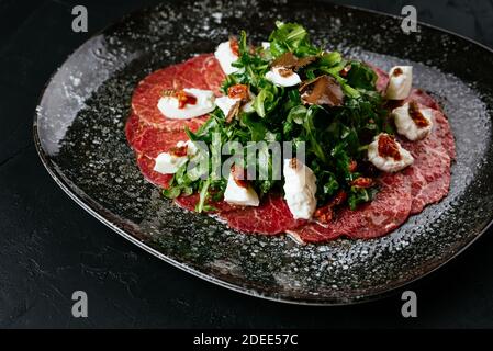 Carpaccio aus Rindfleisch aus Marmor auf schwarzem Hintergrund Stockfoto