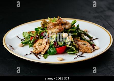 Warmer Salat mit gegrillter Wachtel auf schwarzem Hintergrund Stockfoto