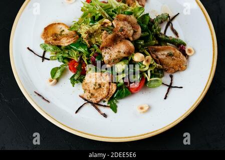 Warmer Salat mit gegrillter Wachtel auf schwarzem Hintergrund Stockfoto