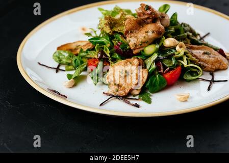 Warmer Salat mit gegrillter Wachtel auf schwarzem Hintergrund Stockfoto