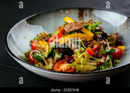 Warmer Salat mit marmorierten Rindersteaks auf schwarzem Hintergrund Stockfoto