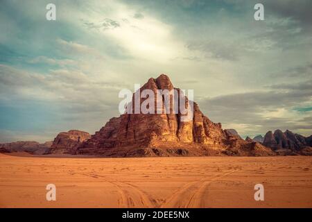 Jabal al-Mazmar, bekannt als die sieben Säulen der Weisheit, in der Wüste Wadi Rum, Jordanien, mit Reifenspuren im Sand. Stockfoto