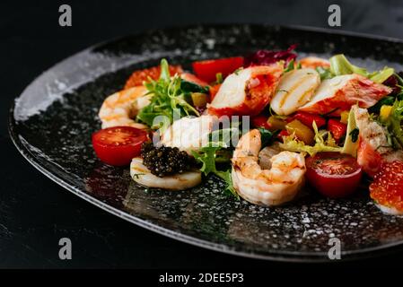 Salat mit Garnelen, Gemüse und Krabbenfleisch auf schwarzem Hintergrund Stockfoto