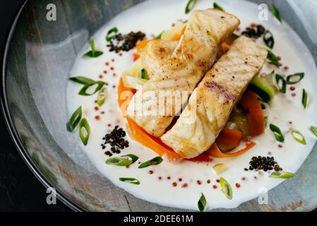Gegrilltes Kabeljaufilet mit Gemüse und Sauce auf einem schwarzen Hintergrund Stockfoto