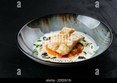 Gegrilltes Kabeljaufilet mit Gemüse und Sauce auf einem schwarzen Hintergrund Stockfoto