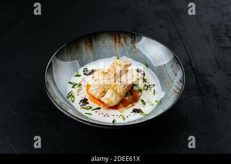 Gegrilltes Kabeljaufilet mit Gemüse und Sauce auf einem schwarzen Hintergrund Stockfoto