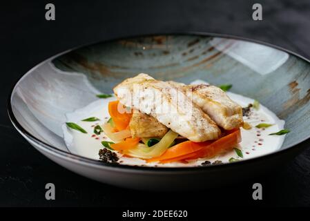 Gegrilltes Kabeljaufilet mit Gemüse und Sauce auf einem schwarzen Hintergrund Stockfoto