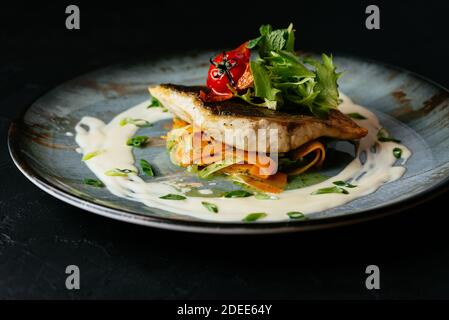 Gegrilltes Kabeljaufilet mit Gemüse und Sauce auf einem schwarzen Hintergrund Stockfoto