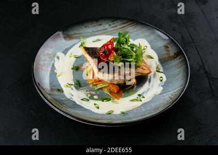 Gegrilltes Kabeljaufilet mit Gemüse und Sauce auf einem schwarzen Hintergrund Stockfoto