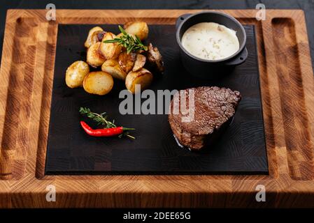 Marmoriertes Rindersteak mit Gemüse und Sauce auf einem schwarzen Hintergrund Stockfoto