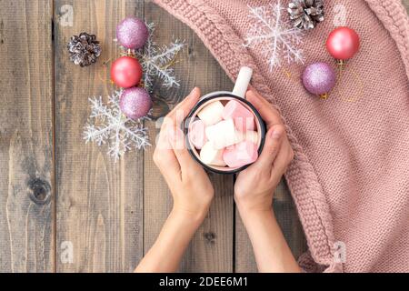 Frauen Hände halten Tasse mit heißem Kaffee mit Schaum und Marshmallows auf der Holztisch.das Konzept der Winter, Wärme, Urlaub und Veranstaltungen.Weiche Fokus. Stockfoto