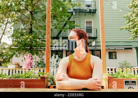 Junge Frau, die in einem Outdoor-Restauranttisch sitzt und Gesichtsmask trägt. Stockfoto