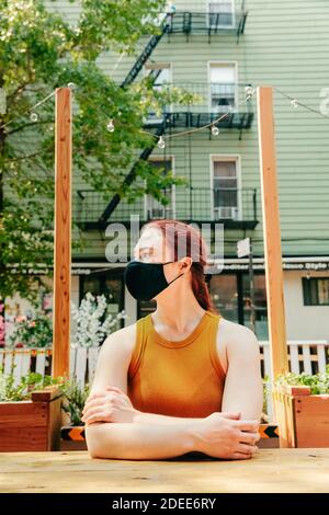 Junge Frau, die in einem Outdoor-Restauranttisch sitzt und Gesichtsmask trägt. Stockfoto