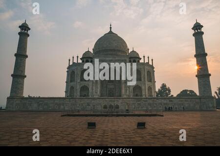 Taj Mahal Westseite gegen bewölkten Himmel und Sonne Peaking auf einem der Minarette, während Sonnenaufgang Zeit, Agra, Indien Stockfoto