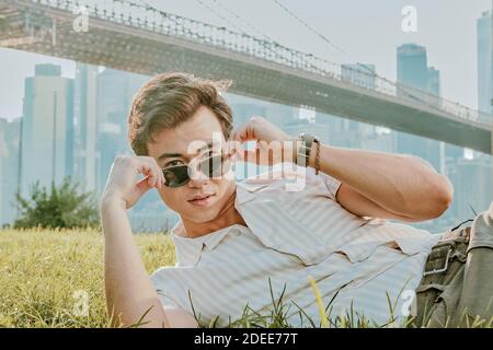 Junger Mann, der draußen im Park sitzt und eine Sonnenbrille trägt. Stockfoto