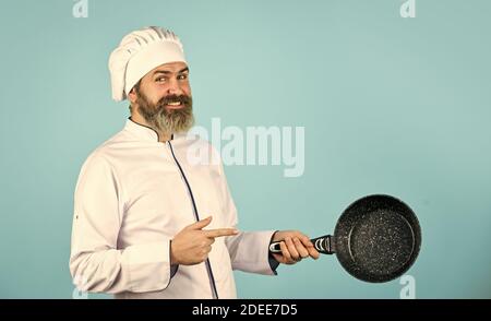 Antihaftbeschichtetes Kochgeschirr. Frittieren ohne Öl. Professionelle küchengeräte. Antihaftpfanne zum Frittieren. Emaillierte Kochgefäße. Mann halte die Pfanne. Frittiermahlzeit. Gesunde Ernährung. Bärtiger Koch bereitet Frühstück zu. Stockfoto