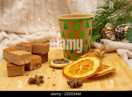 Einweg-Weihnachtsglas aus Pappe mit einem Getränk und verschiedenen Süßigkeiten und aromatischen Gewürzen auf einem Holztablett. Stockfoto