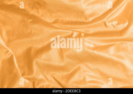 Glänzend Satin Seide Stoff mit Falten Hintergrund Textur Textil. Getönt in 2021 Farbe orange Ringelblume Stockfoto