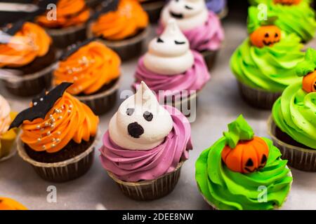 Bunte Kuchen für Halloween. Ein Set festlicher Cupcakes und Leckereien mit Streuseln und Süßigkeiten in einer Konditorei. Hintergrund einer Vielzahl von ch Stockfoto