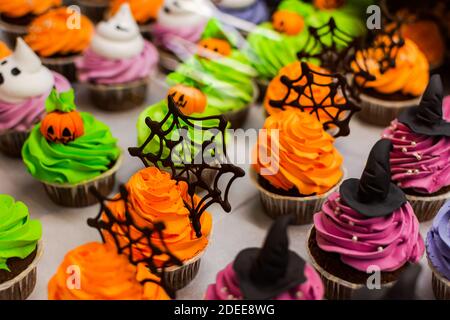 Bunte Kuchen für Halloween. Ein Set festlicher Cupcakes und Leckereien mit Streuseln und Süßigkeiten in einer Konditorei. Hintergrund einer Vielzahl von ch Stockfoto