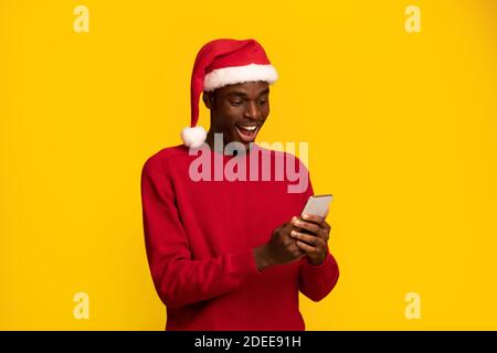 Überrascht schwarzen Kerl in weihnachten santa Hut Blick auf Smartphone Angezeigt Stockfoto