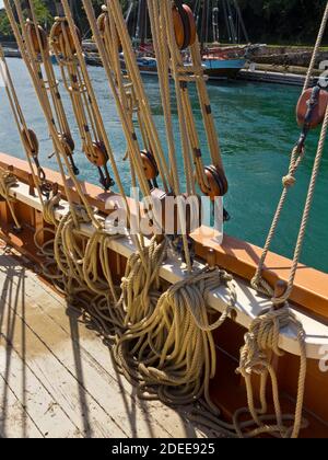 Nahaufnahme von Seilen und Takelage auf einem Segelschiff mit dem Holzdeck im Vordergrund sichtbar. Stockfoto