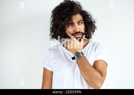 Porträt nachdenklicher junger arabischer arabischer Mann isoliert im Studio, lockig dunkelhaariger Mann denkt über Frage, nachdenklichen Ausdruck. Zweifel konz Stockfoto