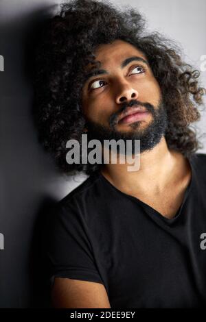 Verträumt lockigen arabischen Mann suchen nach oben, bärtigen Kerl ist über etwas denken, isoliert schwarzen Hintergrund Stockfoto