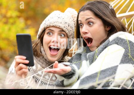 Zwei überraschte Freunde überprüfen gemeinsam Smartphone-Inhalte im Herbst Urlaub Stockfoto