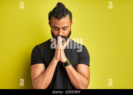 Calm arabisch Kerl betet isoliert auf grünem Hintergrund im Studio. Schöner Kerl halten die Hände zusammen, mit geschlossenen Augen Stockfoto
