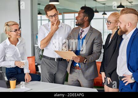 Multi-ethnisch freundliches Team von Kollegen reden Projekte diskutieren, schwarze Männer halten Papier in den Händen, geben Anweisungen Stockfoto