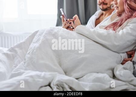 Paar mit Smartphones in Pyjamas auf ihrem Bett, kaukasischen Mann und Frau suchen oder im Internet surfen und SMS im Chat mit anderen Menschen Stockfoto