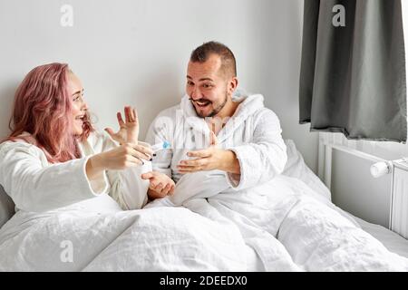 Mann glücklich reagieren auf Test der Schwangerschaft, freudiges Paar, das Ergebnisse eines Schwangerschaftstests zu Hause auf dem Bett liegend herausfindet Stockfoto